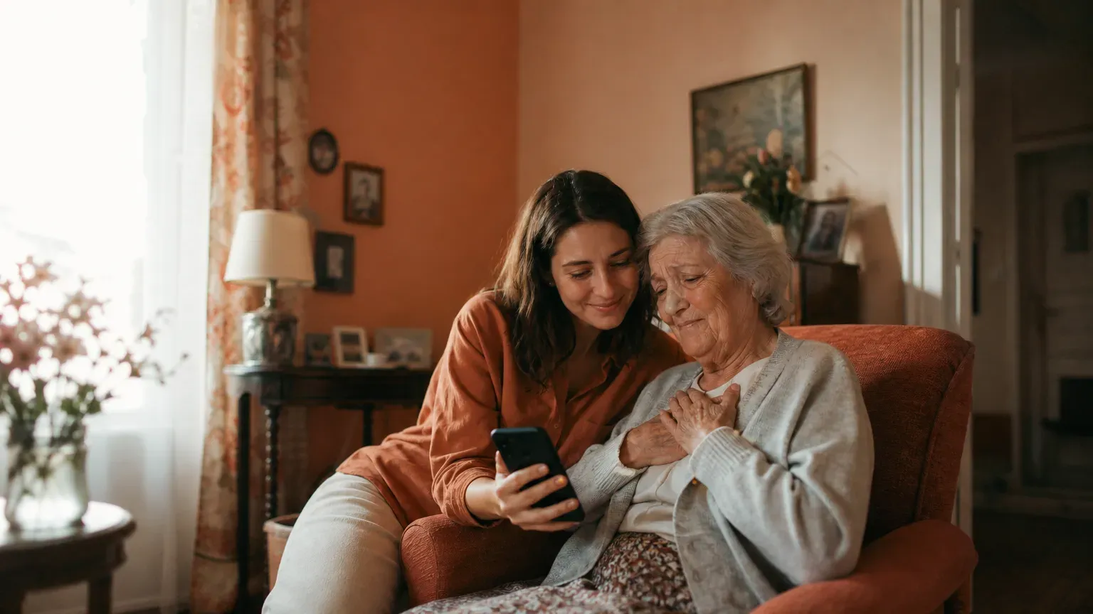 Une grand-mère écoute une chanson sur le téléphone que lui tend sa petite-fille, dans son salon
